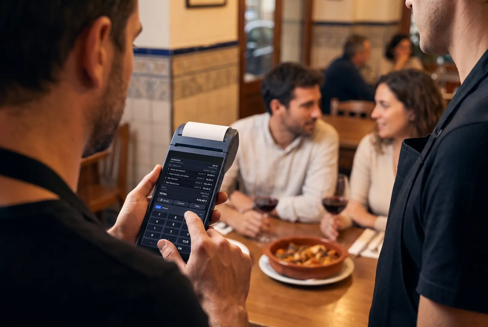 Un camarero toma nota en una comandera con el software de Balles junto a la mesa de una pareja